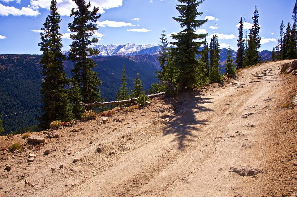 A dirt road climbing through spruce toward Hagerman Pass with distant peaks